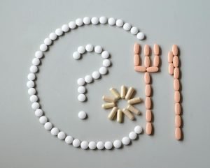 Artistic layout of various pills forming a question mark with fork and sun.